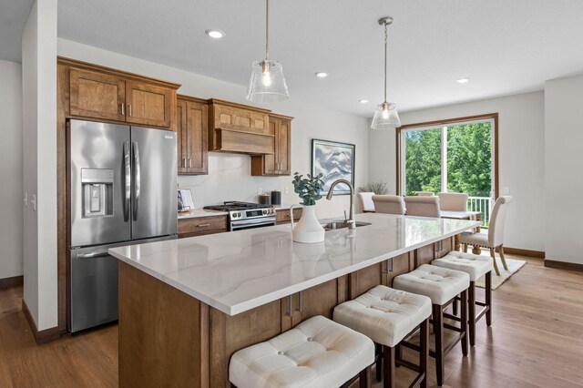 kitchen featuring stainless steel appliances, light wood-type flooring, and an island with sink