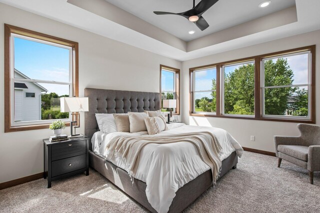 carpeted bedroom with ceiling fan and a raised ceiling