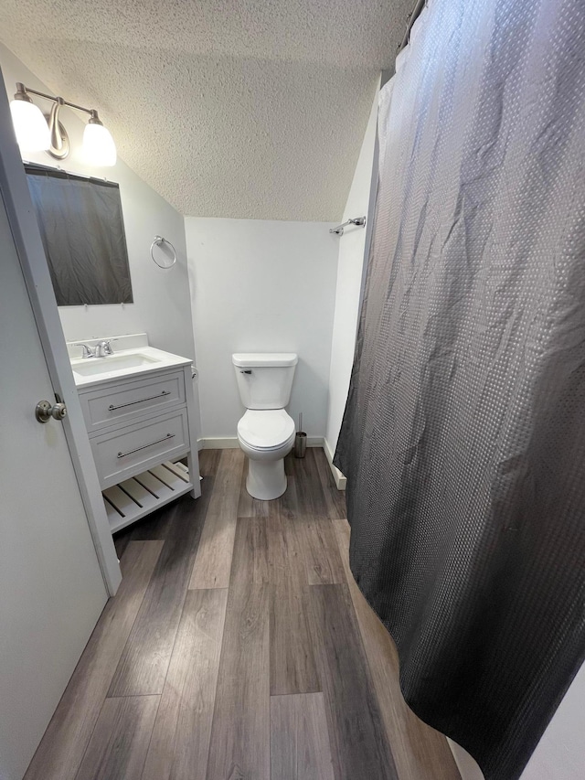 bathroom with wood-type flooring, a textured ceiling, a shower with curtain, vanity, and toilet