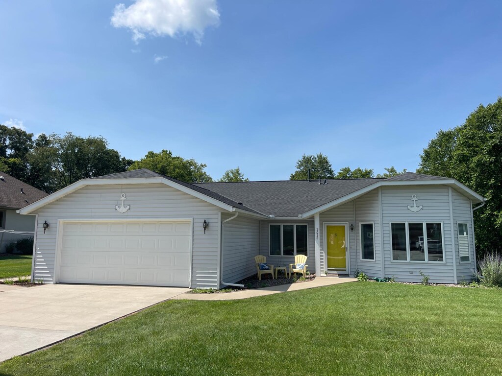 ranch-style home with driveway, an attached garage, a shingled roof, and a front yard