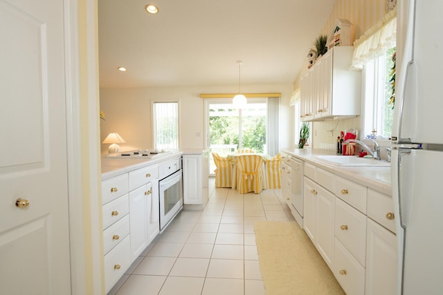 kitchen featuring white appliances, sink, pendant lighting, light tile patterned floors, and white cabinetry