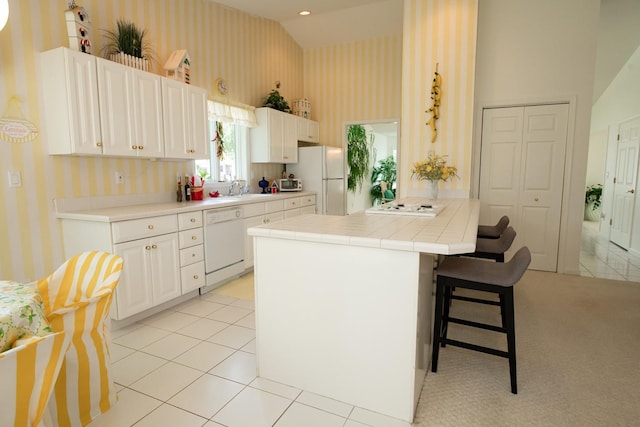 kitchen featuring tile counters, white appliances, light tile patterned floors, sink, and high vaulted ceiling