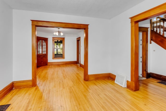 empty room featuring an inviting chandelier and light hardwood / wood-style flooring