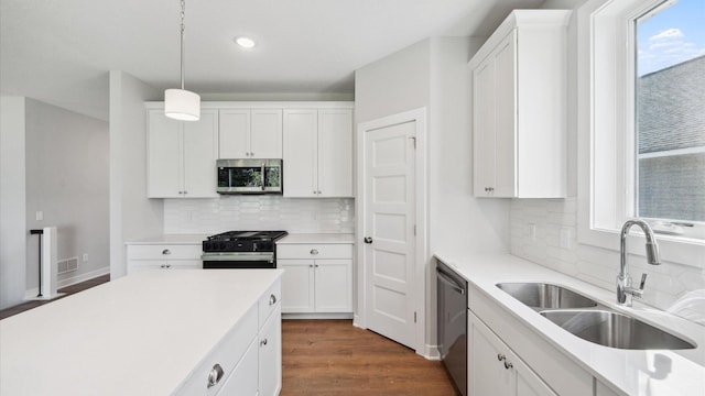 kitchen featuring appliances with stainless steel finishes, pendant lighting, dark wood-type flooring, sink, and white cabinetry