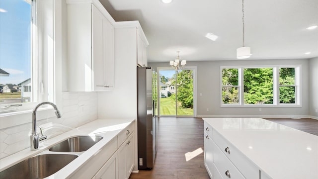 kitchen with sink, white cabinetry, stainless steel refrigerator, pendant lighting, and a notable chandelier