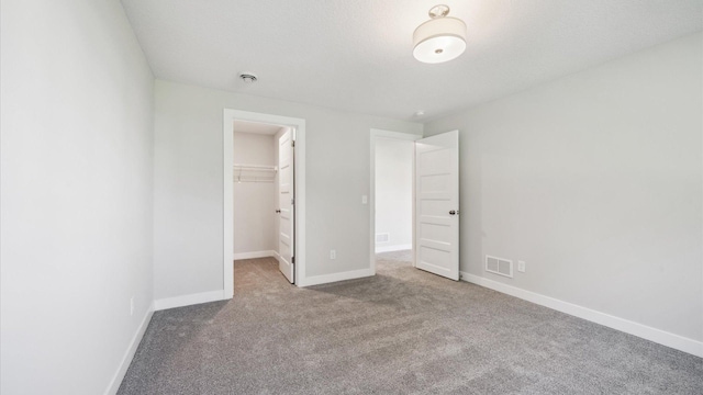 unfurnished bedroom with a walk in closet, a closet, and light carpet