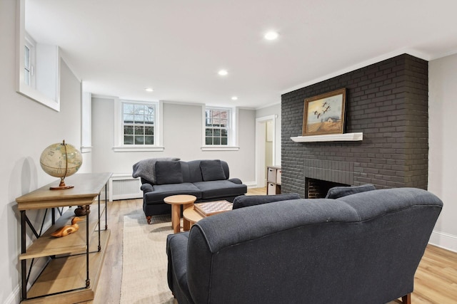 living room featuring a brick fireplace, radiator, and light hardwood / wood-style flooring