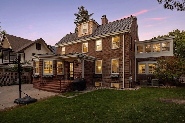 back house at dusk featuring a yard, central AC unit, and a patio area