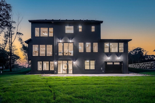 back house at dusk featuring a lawn