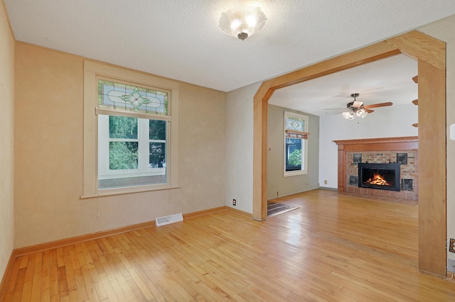 unfurnished living room with a fireplace, ceiling fan, a textured ceiling, and light wood-type flooring