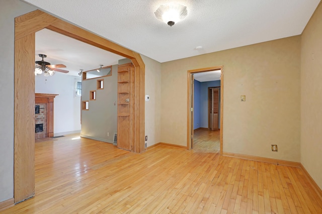 empty room with ceiling fan, a fireplace, a textured ceiling, and light hardwood / wood-style flooring