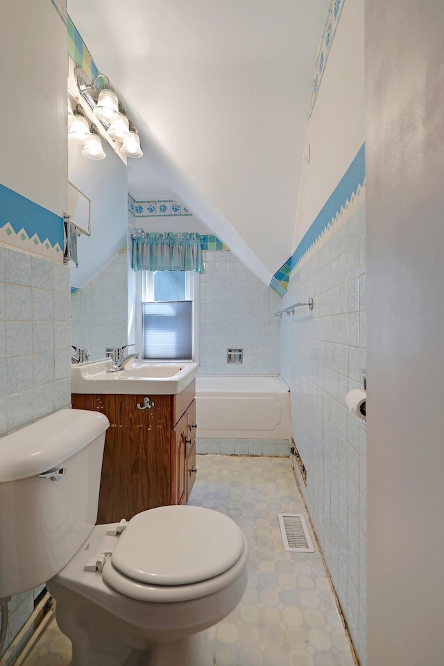 full bathroom with toilet, vanity, tile patterned flooring, tile walls, and vaulted ceiling