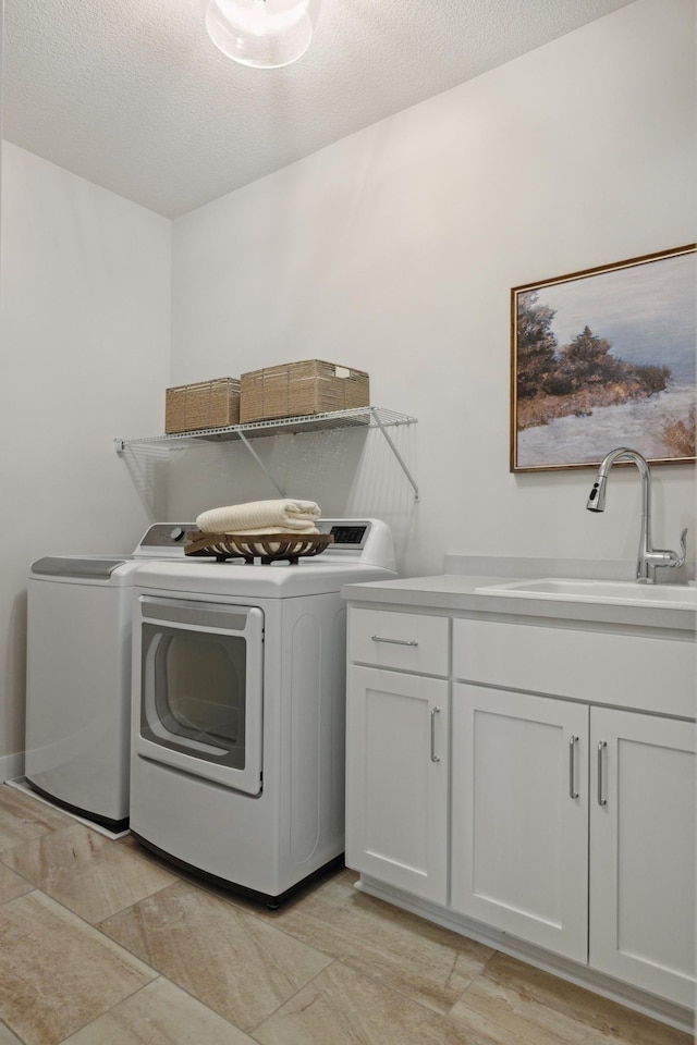 laundry room with cabinets, washing machine and clothes dryer, sink, and a textured ceiling