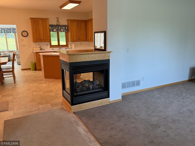 kitchen featuring light colored carpet, a multi sided fireplace, decorative light fixtures, and a wealth of natural light