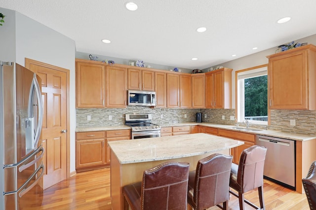 kitchen with light wood-type flooring, a center island, tasteful backsplash, sink, and appliances with stainless steel finishes