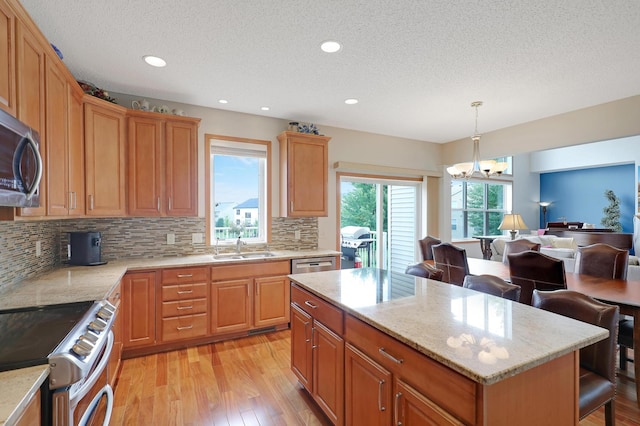 kitchen with appliances with stainless steel finishes, hanging light fixtures, a center island, light hardwood / wood-style flooring, and a notable chandelier