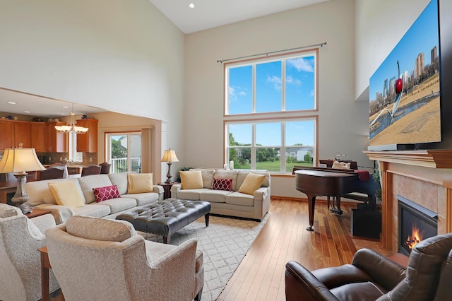 living room featuring a towering ceiling, a chandelier, a tile fireplace, and light wood-type flooring