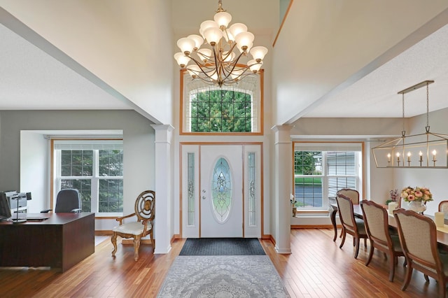 foyer entrance featuring wood-type flooring, an inviting chandelier, a towering ceiling, and ornate columns