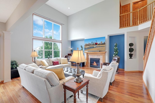 living room featuring light hardwood / wood-style floors, a towering ceiling, and a tiled fireplace