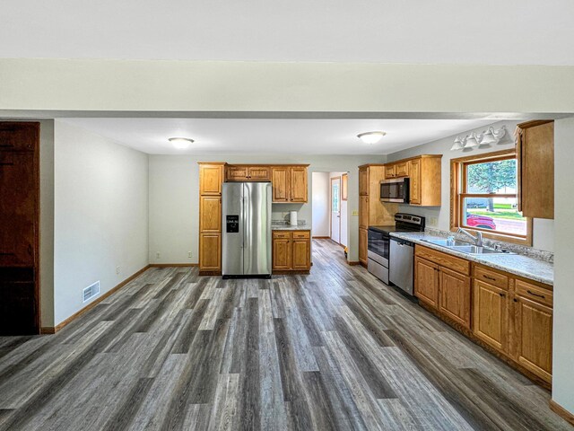 kitchen featuring stainless steel appliances, light stone counters, sink, and dark wood-type flooring