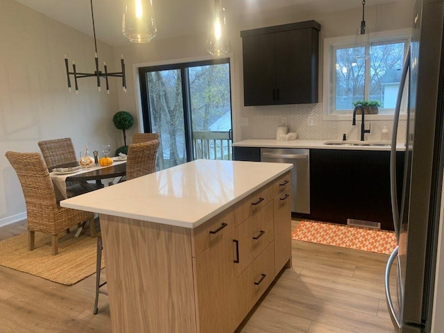 kitchen with light wood-type flooring, appliances with stainless steel finishes, a center island, and hanging light fixtures