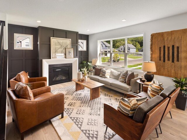 living area with light wood-style floors, a decorative wall, a glass covered fireplace, and recessed lighting