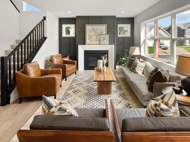 living area with healthy amount of natural light, stairs, light wood finished floors, recessed lighting, and a glass covered fireplace