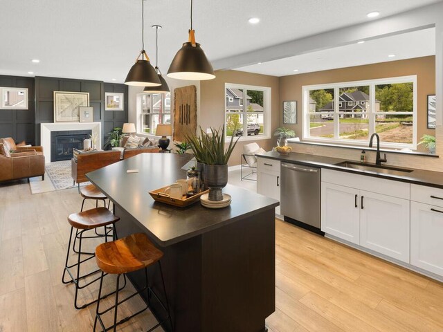 kitchen featuring dishwasher, dark countertops, a sink, light wood-style flooring, and white cabinetry