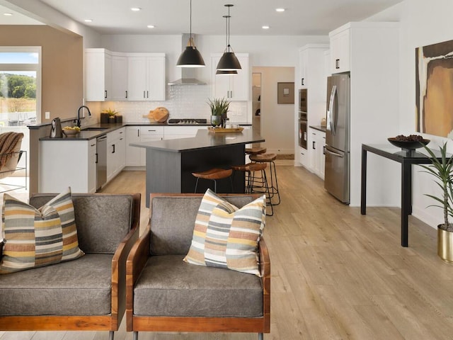 kitchen with white cabinets, stainless steel appliances, sink, light hardwood / wood-style floors, and decorative light fixtures