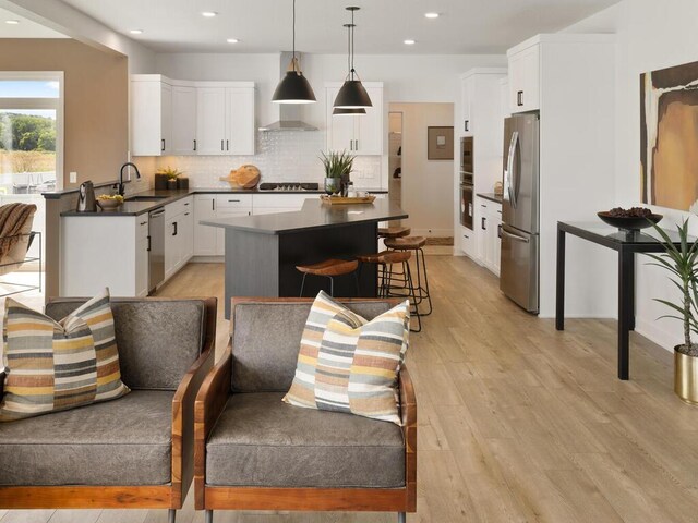 kitchen featuring appliances with stainless steel finishes, a sink, dark countertops, light wood finished floors, and recessed lighting