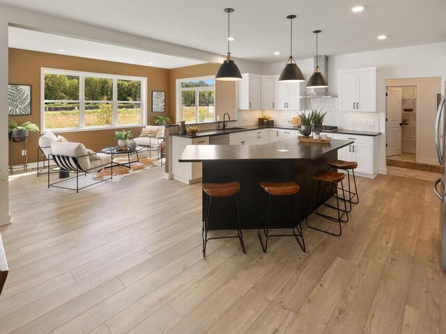 kitchen with a sink, wall chimney range hood, light wood finished floors, dark countertops, and tasteful backsplash