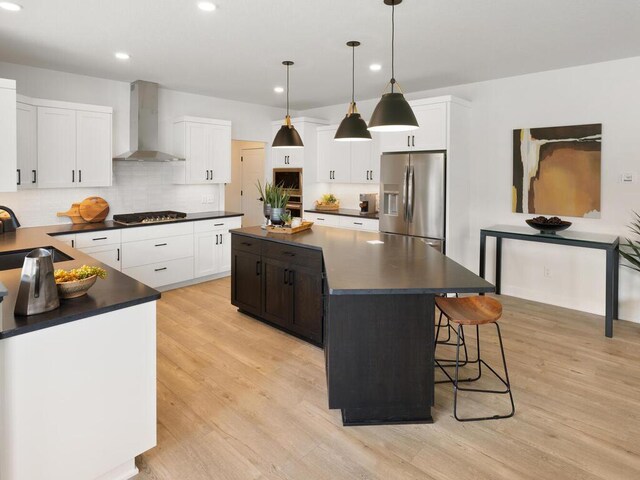 kitchen with wall chimney exhaust hood, stainless steel appliances, a sink, dark countertops, and a center island