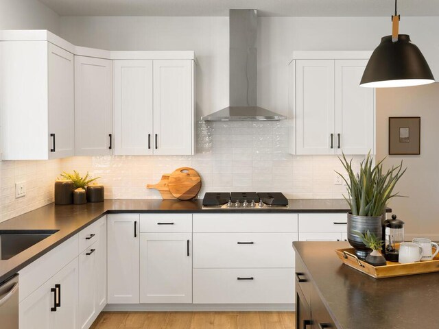 kitchen featuring wall chimney exhaust hood, gas stovetop, dark countertops, and white cabinets