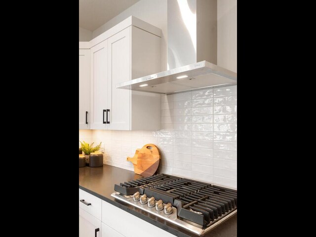 kitchen featuring wall chimney range hood, stainless steel gas stovetop, decorative backsplash, white cabinetry, and dark countertops