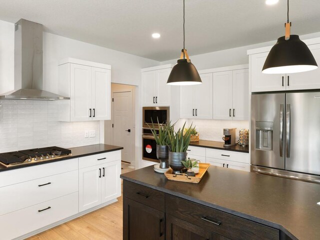 kitchen with appliances with stainless steel finishes, wall chimney range hood, dark countertops, backsplash, and recessed lighting
