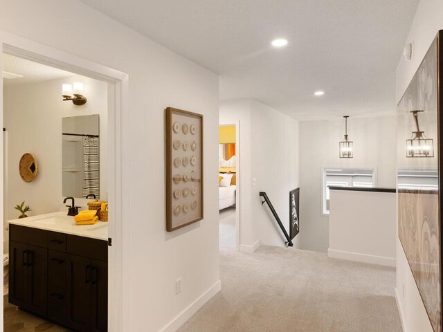 hall with an upstairs landing, a sink, carpet floors, recessed lighting, and baseboards