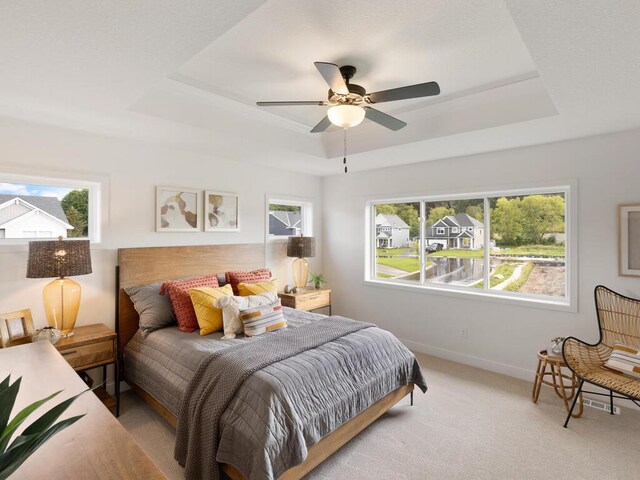 bedroom with a tray ceiling, baseboards, light carpet, and a ceiling fan