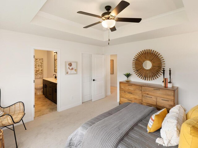 bedroom featuring a raised ceiling, light carpet, baseboards, ensuite bathroom, and ceiling fan