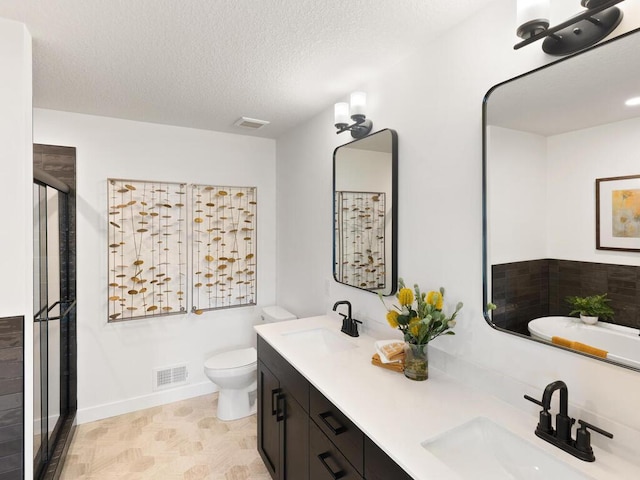 full bath with toilet, a stall shower, a textured ceiling, double vanity, and baseboards