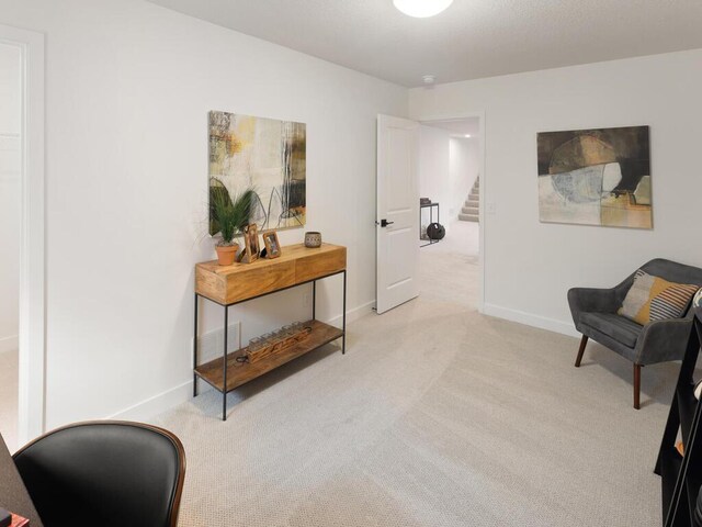 sitting room with light colored carpet, stairway, baseboards, and an office area