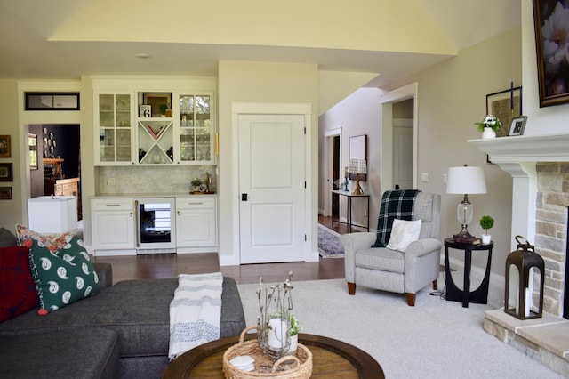 living room featuring indoor bar, a stone fireplace, beverage cooler, and dark wood-type flooring