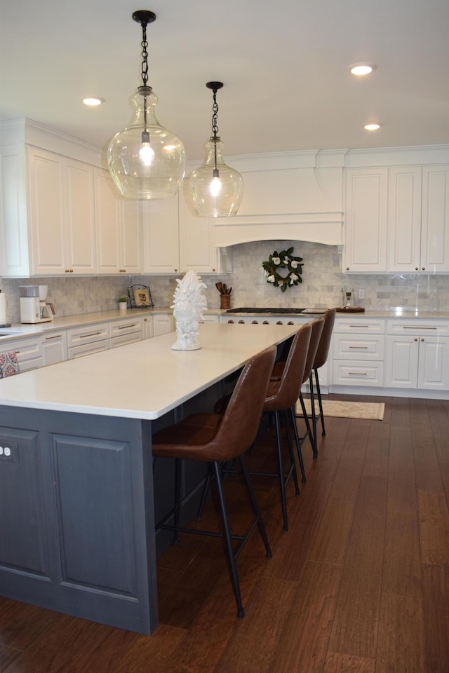 kitchen with dark wood-type flooring, a spacious island, decorative light fixtures, a breakfast bar area, and white cabinets