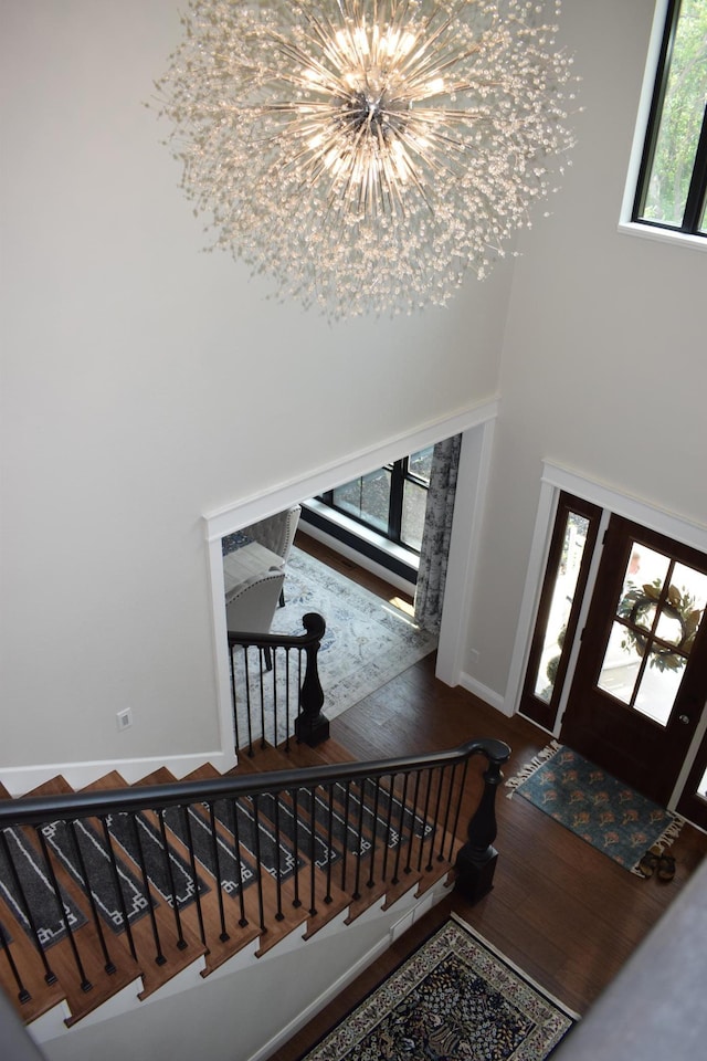 foyer entrance featuring a healthy amount of sunlight, a towering ceiling, dark wood-type flooring, and a chandelier