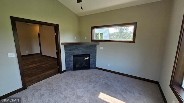 unfurnished living room featuring a stone fireplace, dark carpet, ceiling fan, and lofted ceiling