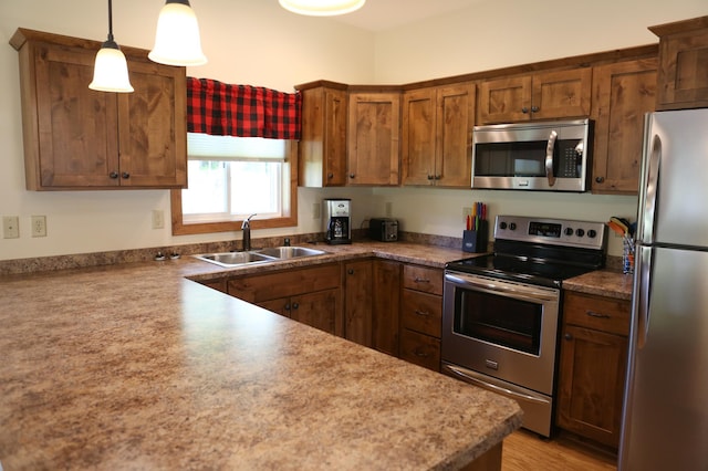 kitchen with stainless steel appliances, decorative light fixtures, light hardwood / wood-style flooring, and sink