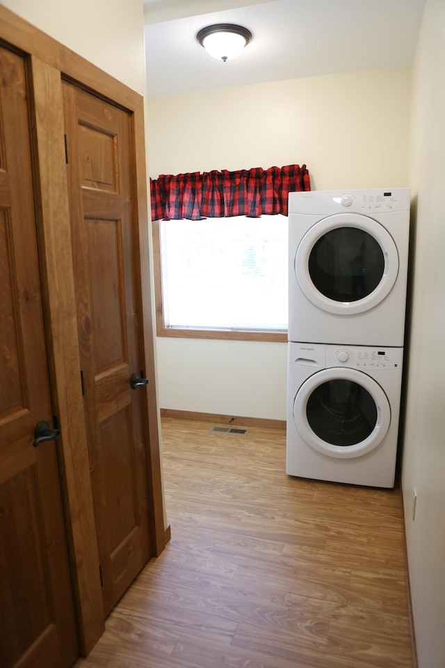 laundry room featuring stacked washer / drying machine and light hardwood / wood-style flooring