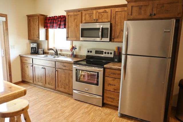 kitchen with appliances with stainless steel finishes, light hardwood / wood-style flooring, and sink