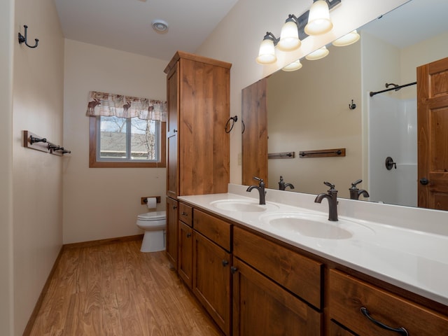 bathroom with toilet, wood-type flooring, and dual bowl vanity