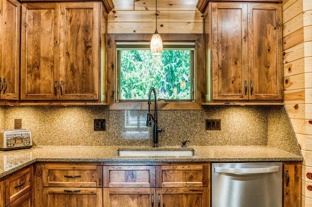 kitchen with a sink, hanging light fixtures, stainless steel dishwasher, brown cabinets, and backsplash