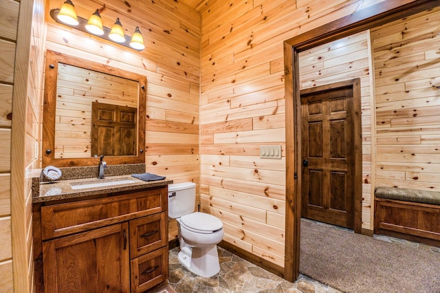 half bath with wooden walls, stone finish flooring, toilet, and vanity